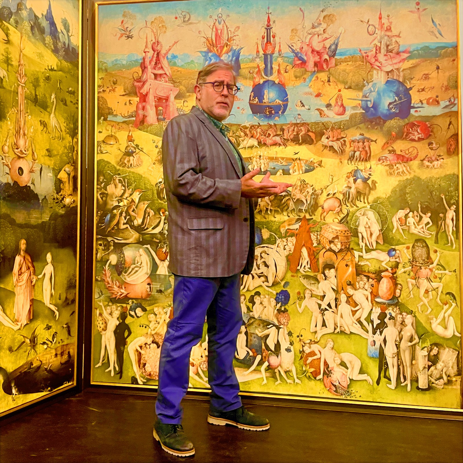 Marc Michael Epstein standing before a full-scale facsimile of Hieronymus Bosch's Garden of Earthly Delights triptych, mid-gesture in lecture.